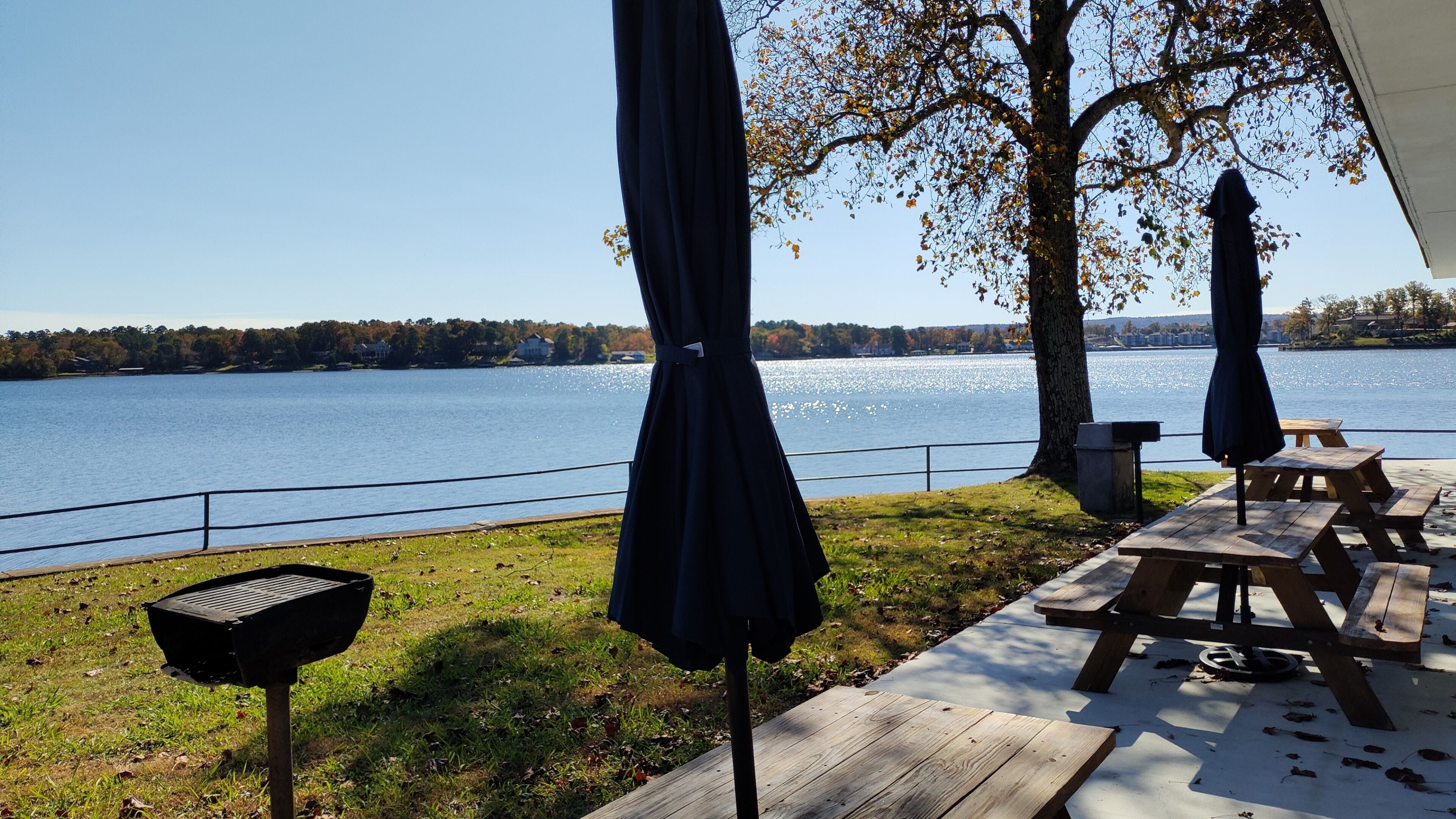 Terraza junto al lago con mesas de picnic y sombrillas, con vista a un lago tranquilo.