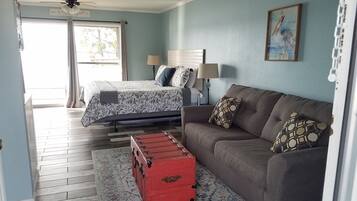 A bedroom with a bed, a sofa, a red trunk, and a window with curtains.