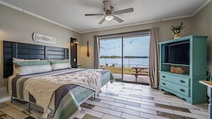 A bedroom with a large bed, a ceiling fan, a TV, and a view of the outdoors. - Willow Beach Resort (Hot Springs)