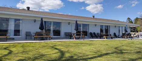 Un bâtiment à la façade en briques, doté de grandes fenêtres et d’un espace extérieur aménagé avec des tables et des chaises.