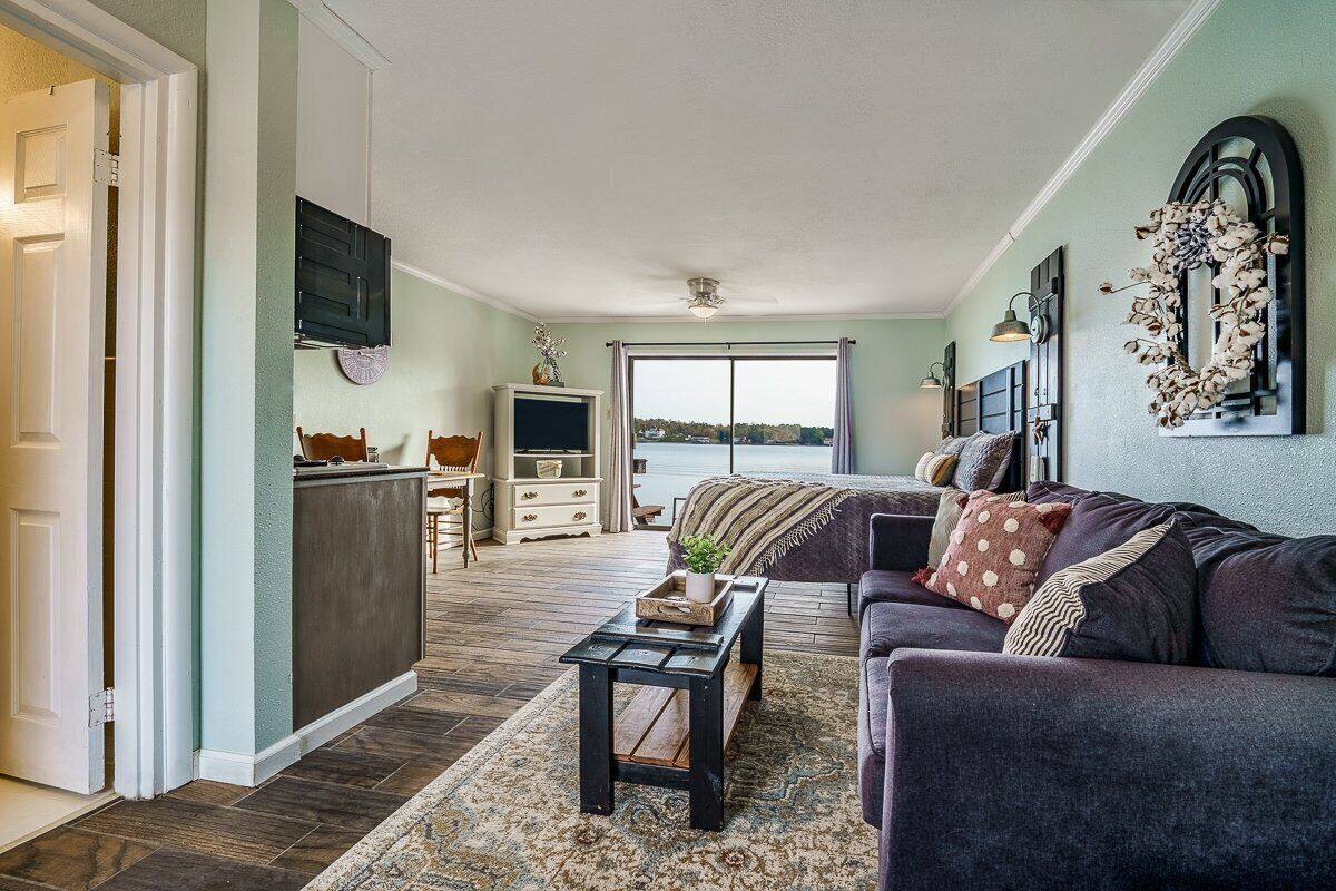 A spacious living room with a large window, a dark-colored sofa, a coffee table, and a television mounted on the wall.