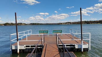 Un muelle de madera con dos bancos verdes y barandillas blancas, que se extiende sobre aguas tranquilas.