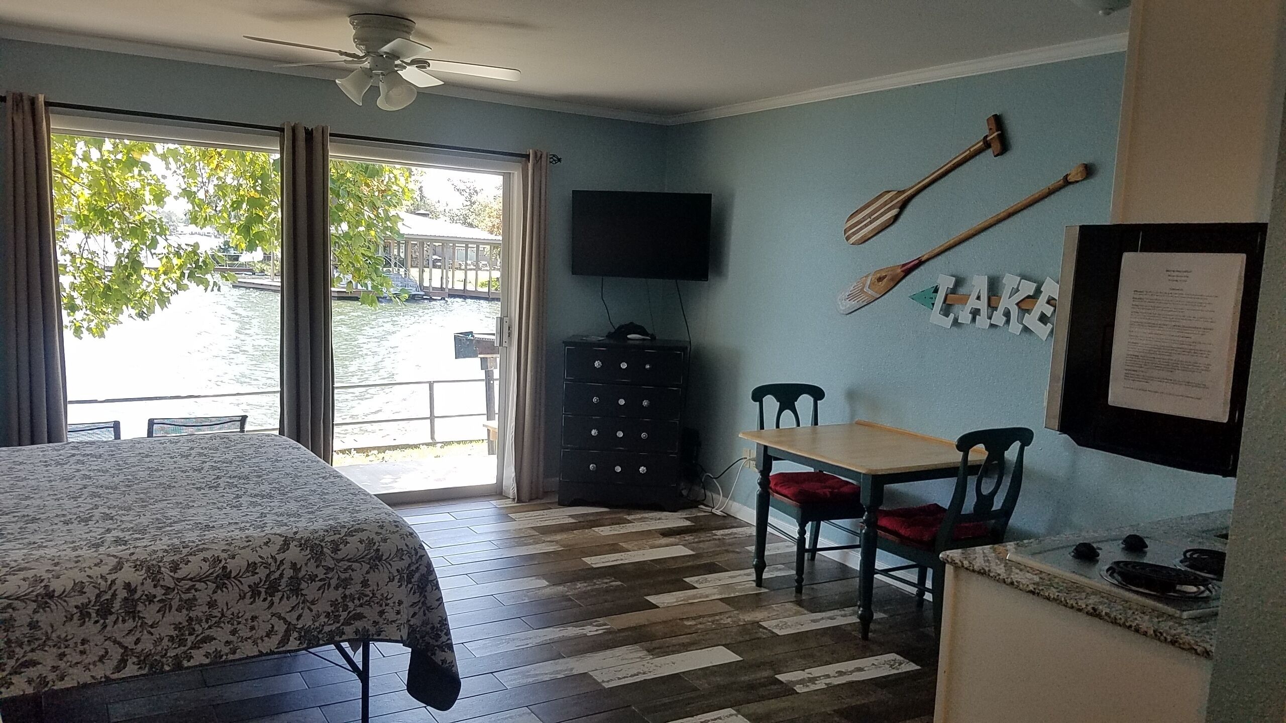 A room with a bed, a desk, a chair, a television, and a view of a body of water through a window.