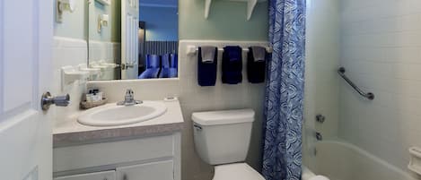 A bathroom with a toilet, sink, and shower. There are towels on a shelf and a shower curtain.