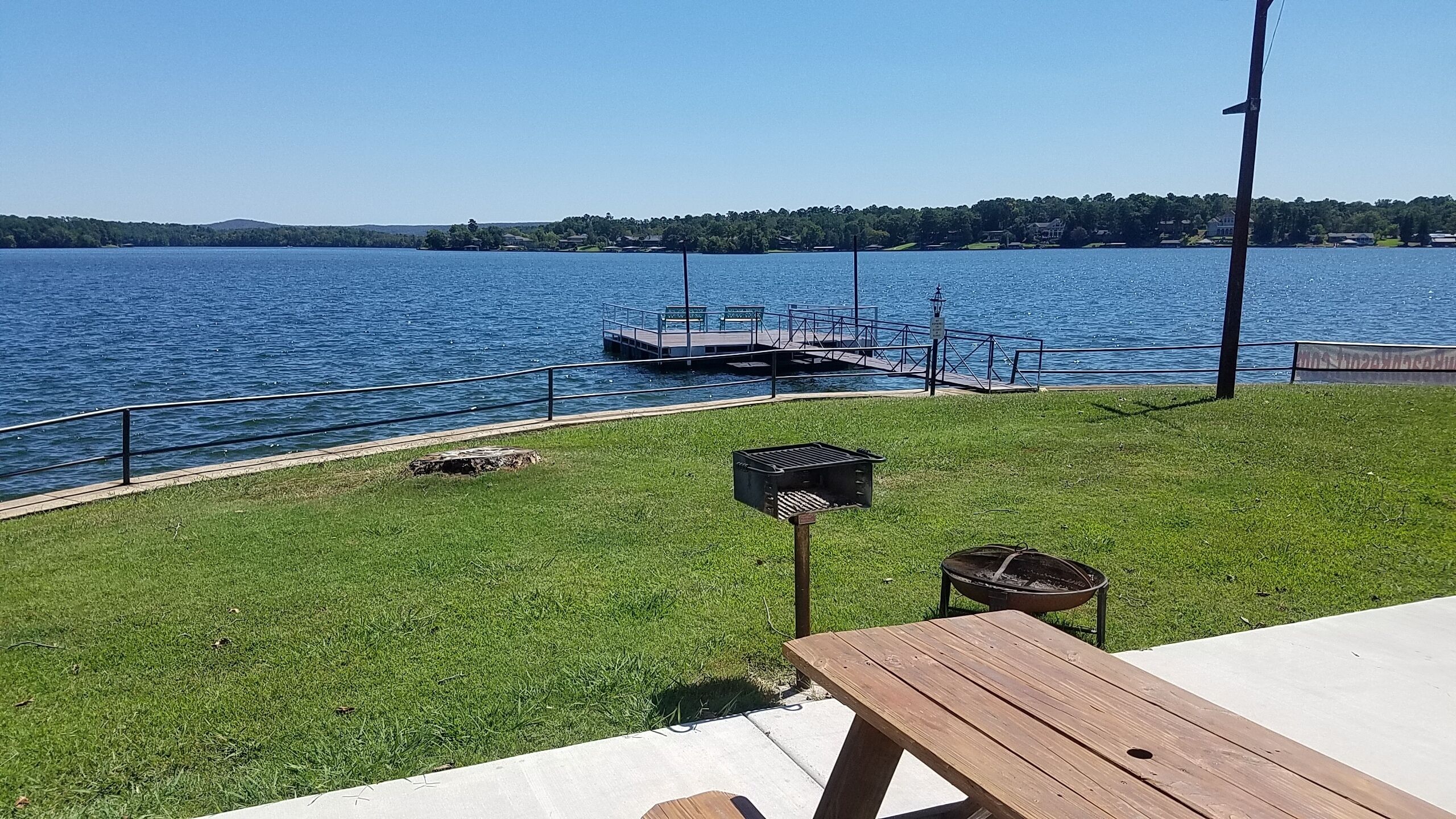 A lakeside view with a dock, grassy area, and picnic table.
