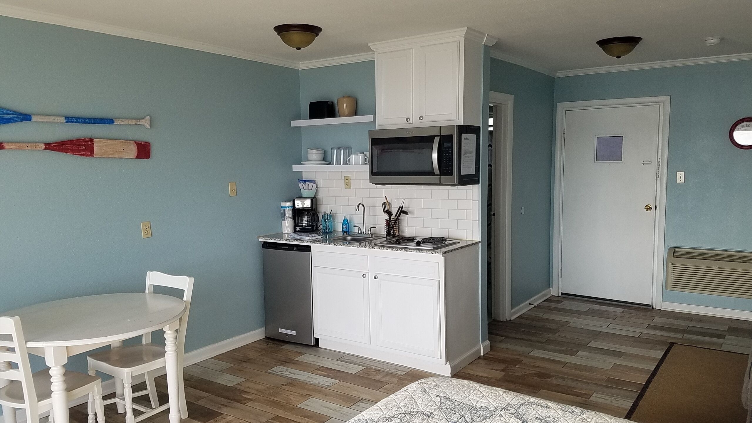 A compact kitchen with white cabinets, a microwave, and a dishwasher. There is a dining table with chairs and a patterned rug.