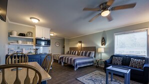 A compact living space with a kitchenette, a dining area, a bedroom with two beds, a sofa, and a ceiling fan. - Willow Beach Resort (Hot Springs)