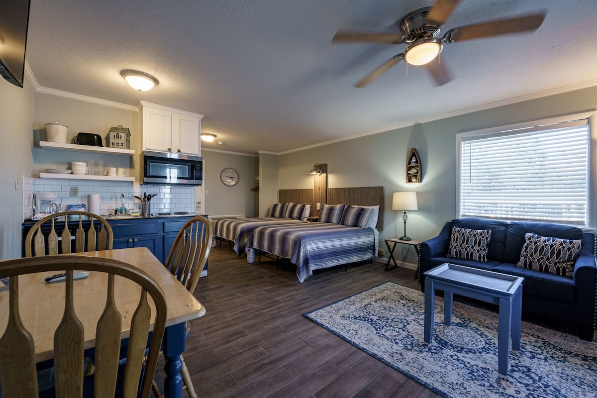 A compact living space with a kitchenette, a dining area, a bedroom with two beds, a sofa, and a ceiling fan.