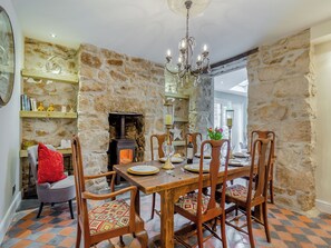 A dining area with a stone wall, a fireplace, wooden chairs, and a chandelier.