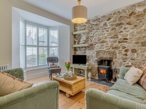 Un salon chaleureux avec un mur en pierre, une cheminée, un téléviseur et des fauteuils confortables.