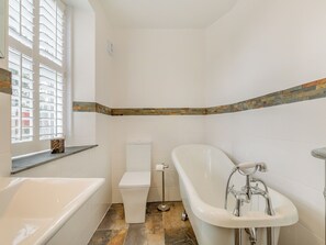 A bathroom with a bathtub, toilet, and window with blinds.