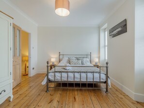 A bedroom with a metal bed frame, two bedside lamps, a wooden floor, and a door leading to another room.