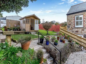 Un jardin agrémenté de plantes en pot, une structure en bois et un bâtiment en pierre.
