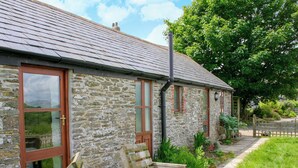 A stone building with a sloped roof, wooden benches, and a garden area. - The Mealhouse-UK12902 (Pelynt, near Looe)