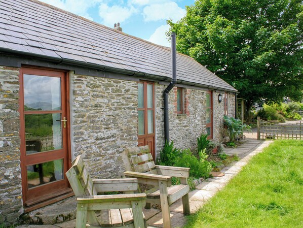 A stone building with a sloped roof, wooden benches, and a garden area.