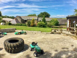 A rural farm setting with a green tractor, a large tire, and a wooden fence.