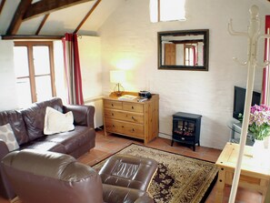 A living room with a sofa, a wooden dresser, a lamp, a television, and a small cabinet.