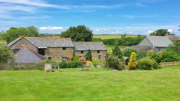A stone building with a sloped roof, surrounded by a grassy field and trees. - The Mealhouse-UK12902 (Pelynt, near Looe)