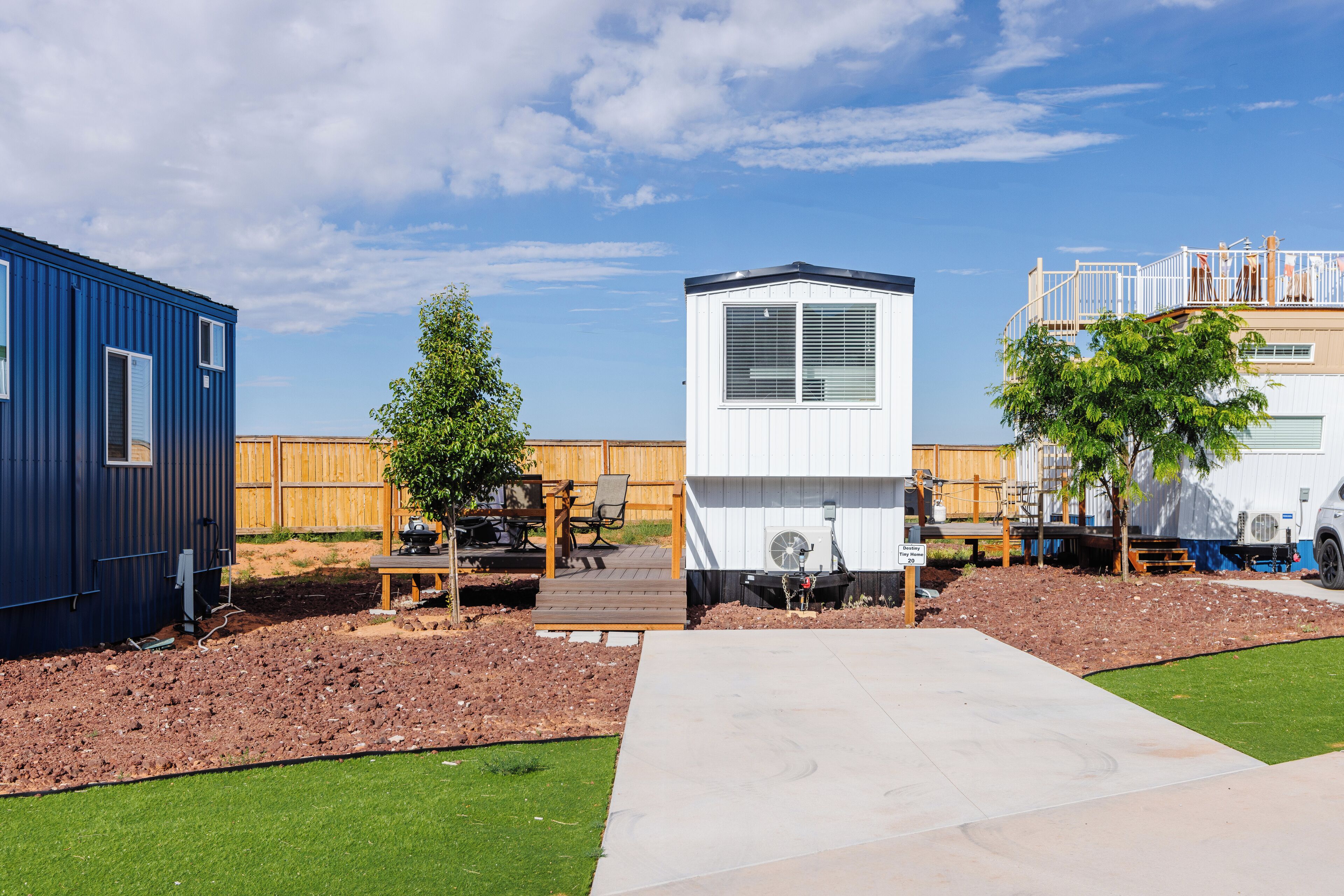 A residential area with a blue mobile home, a white mobile home, and a wooden deck with outdoor furniture.