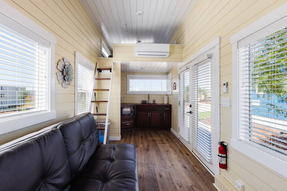 A compact living space with a sofa, kitchenette, and large windows.