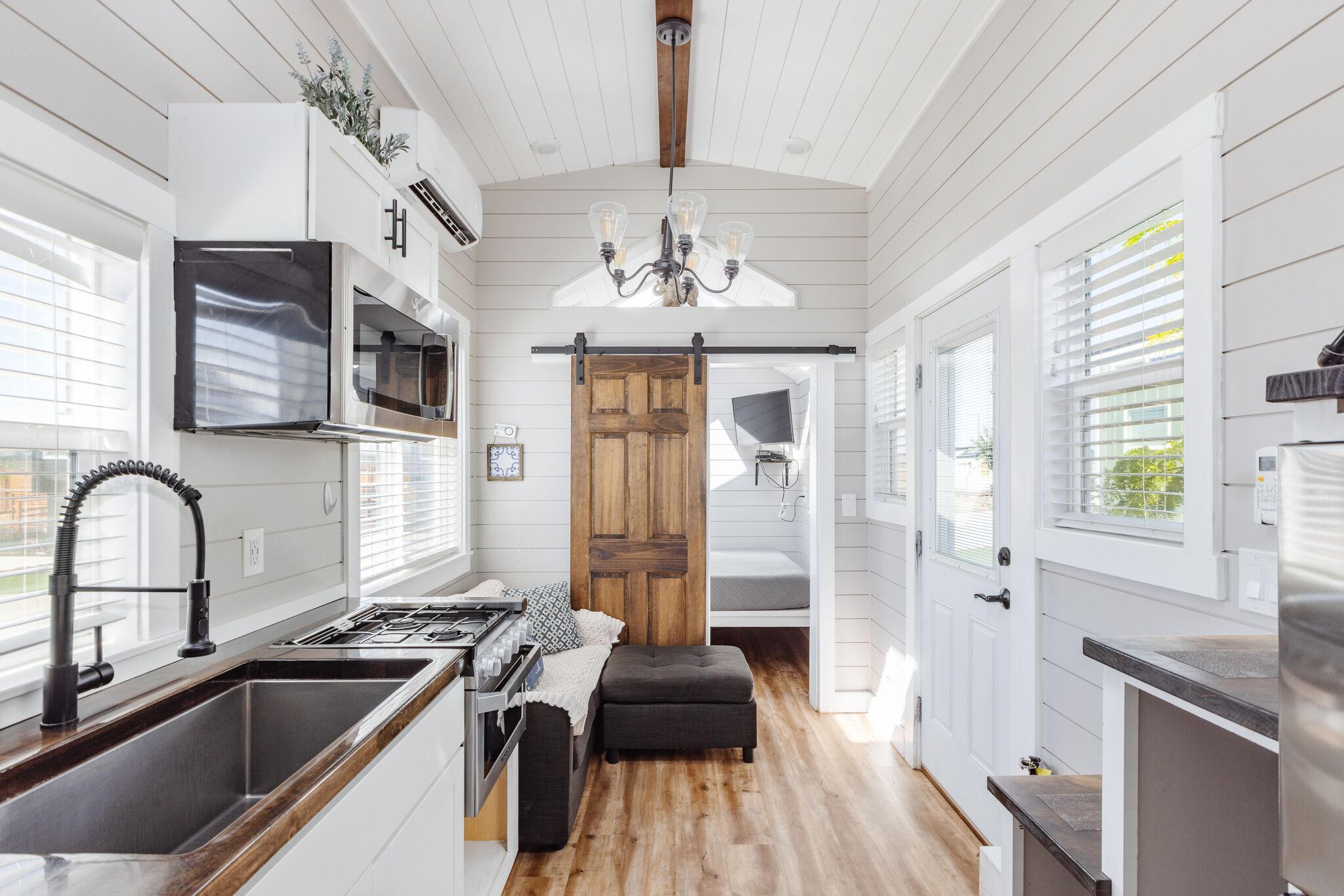 A modern kitchen with a central island, stainless steel appliances, and a wooden door leading to a bedroom.