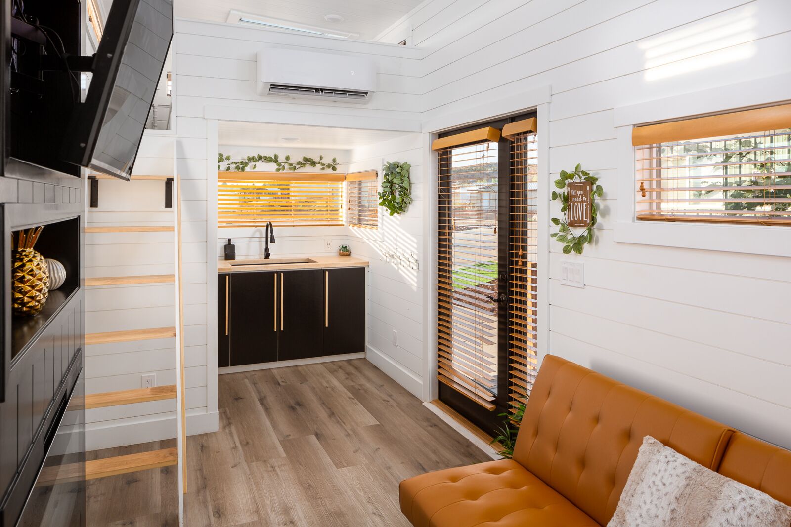 A compact kitchen with a sink, cabinets, and a window with blinds. There's a sofa and a television in the living area.