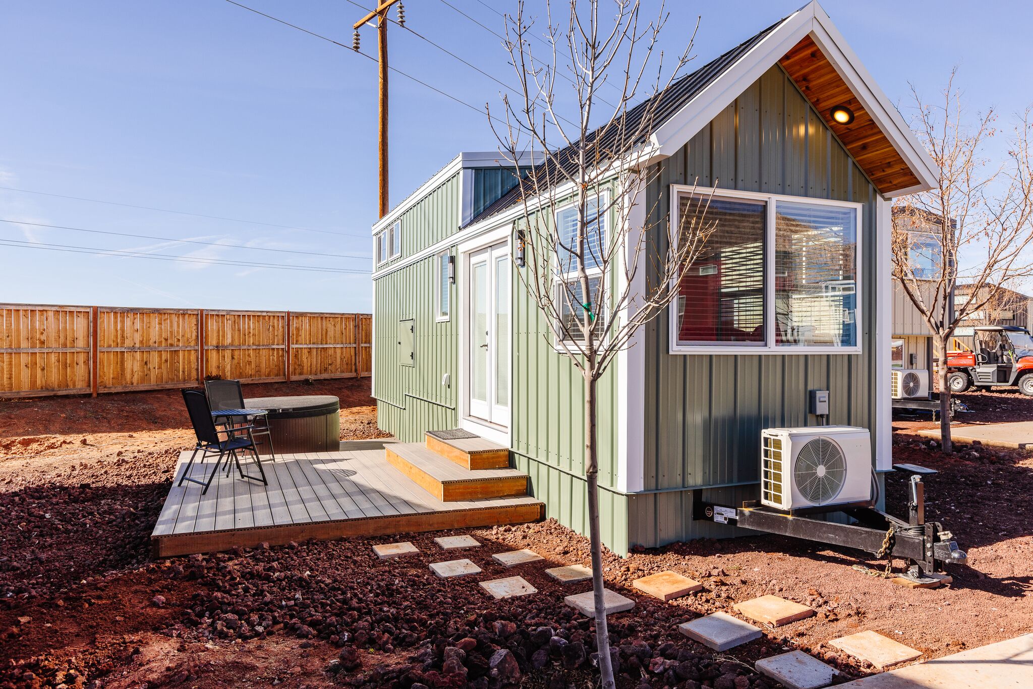 A small, single-story building with a wooden deck, a hot tub, and an air conditioning unit.