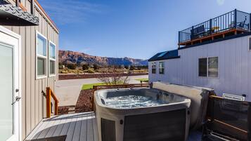A hot tub on a deck with a view of mountains, a balcony, and a sign that says 'Please shower.'