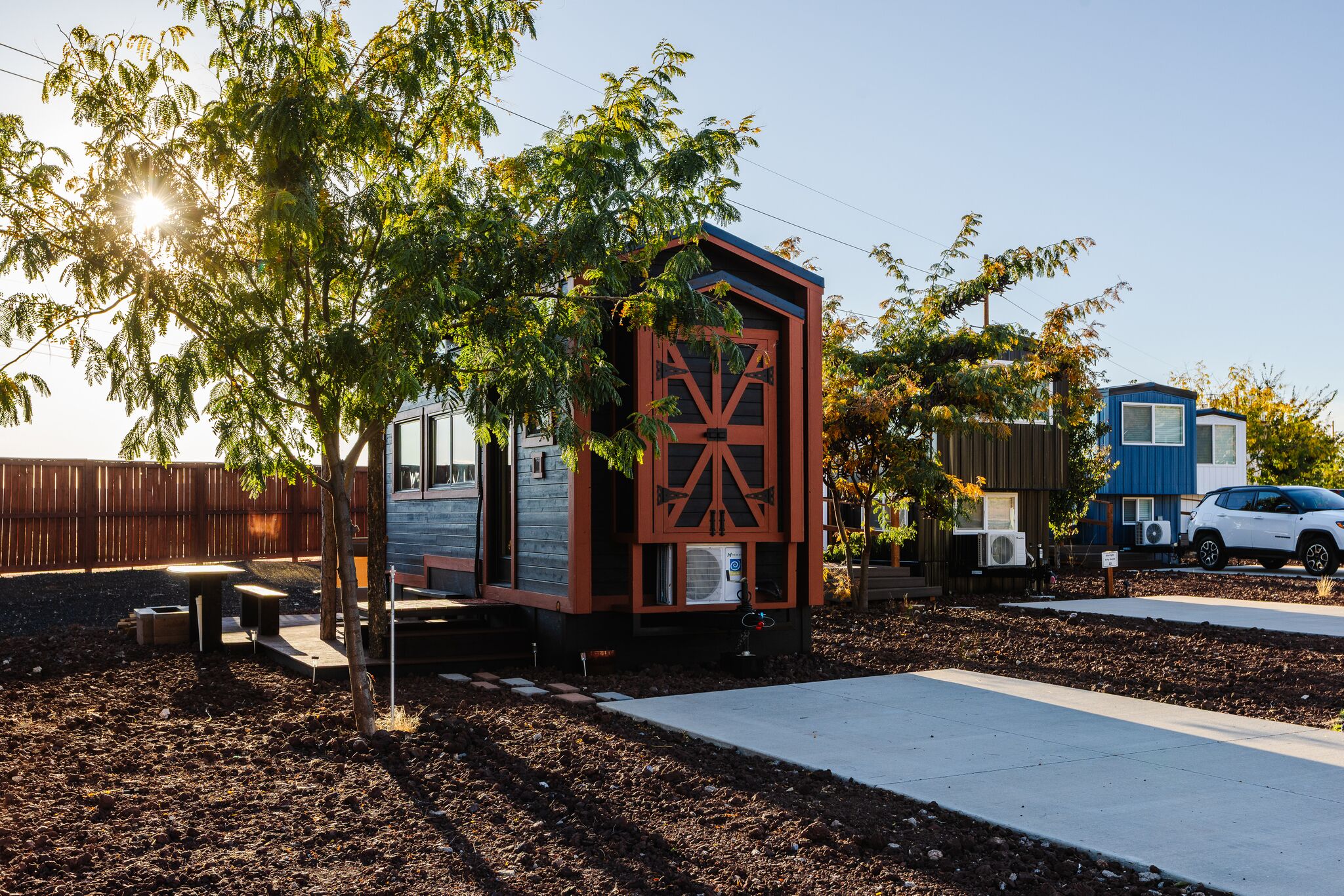A small, single-story building with a distinctive red and black facade, situated in a landscaped area with trees and a paved path.