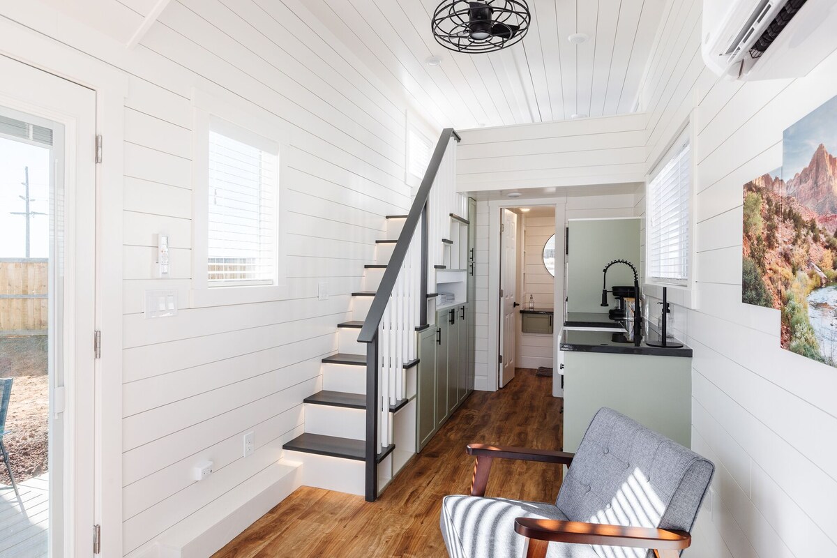 Un interior moderno con paneles blancos, una escalera de madera, una zona de cocina y un espacio para comer.