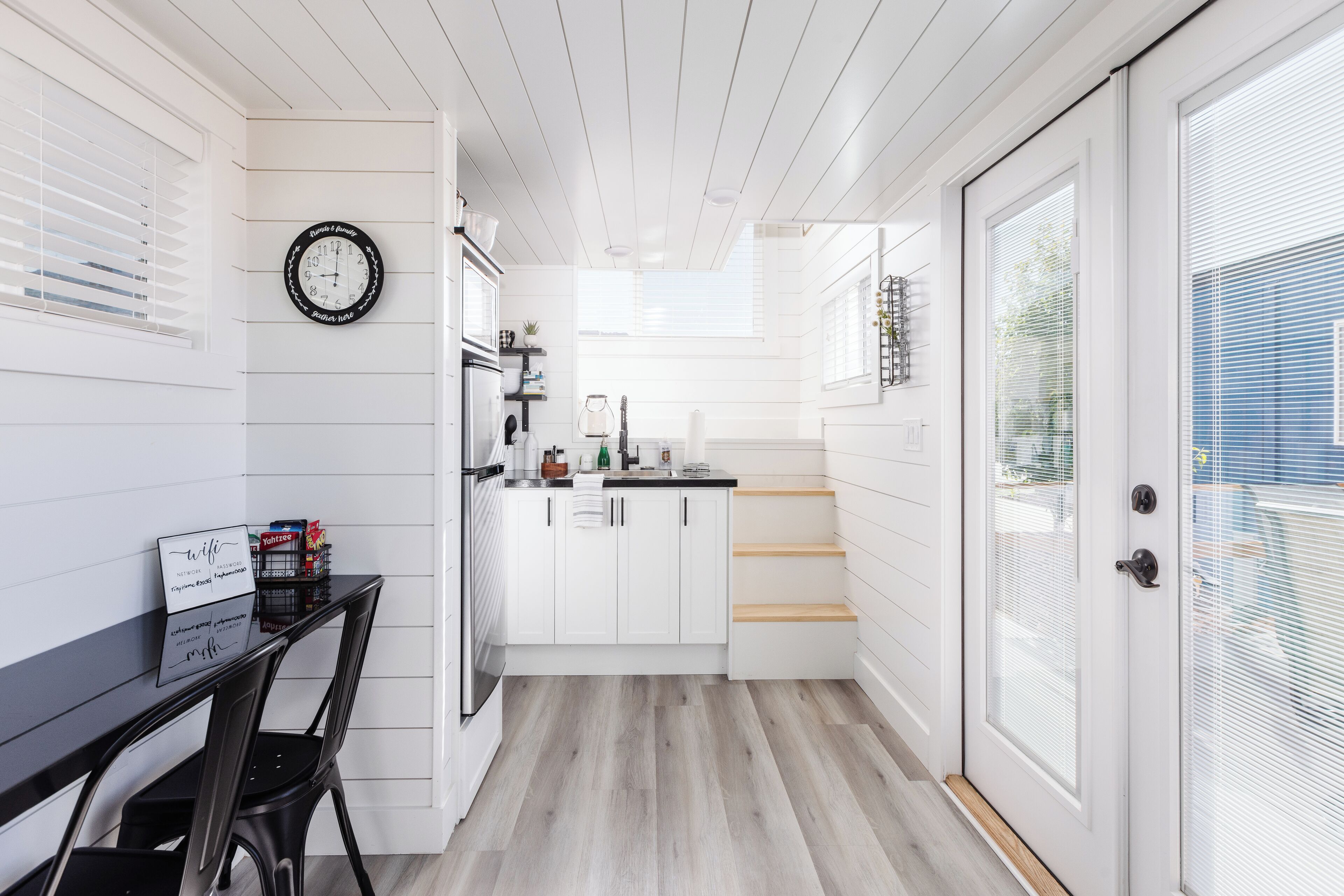 Una cocina moderna con armarios blancos, un reloj negro y un comedor con mesa y sillas negras.