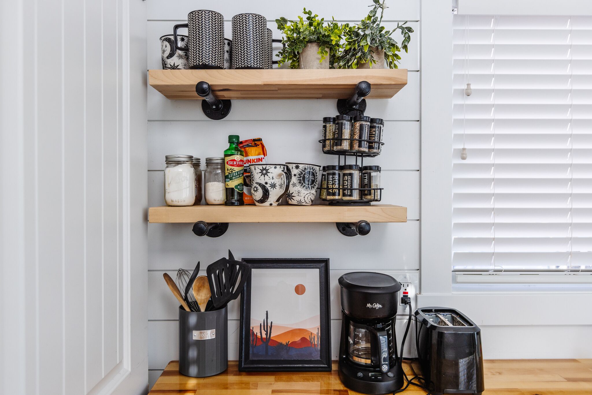 A kitchen with wooden shelves, a coffee maker, a toaster, and a framed picture.