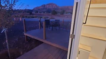 Eine offene Tür, die auf eine Holzterrasse mit Tisch und Stühlen führt, mit Blick auf eine Wüstenlandschaft und einen Berg in der Ferne.