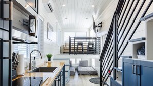 A modern kitchen with a wooden countertop, stainless steel sink, and black cabinets. There is a dining area with a bench and a staircase leading to an upper level. - Zion's Tiny Getaway (Hurricane)