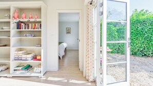 A room with a white bookshelf, a bed with a green blanket, and a view of a garden through an open door. - La Rose - Gillingham, Shaftesbury (West Stour)