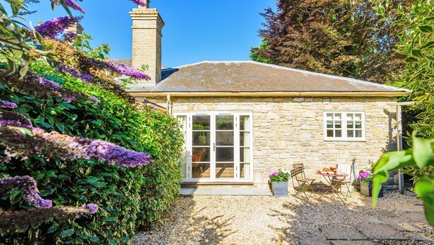 A stone house with a tiled roof, a large glass door, and a small patio with a table and chairs. - La Rose - Gillingham, Shaftesbury (West Stour)
