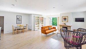 A spacious living area with a wooden floor, a sofa, a dining table with chairs, a bookshelf, and a fireplace. - La Rose - Gillingham, Shaftesbury (West Stour)