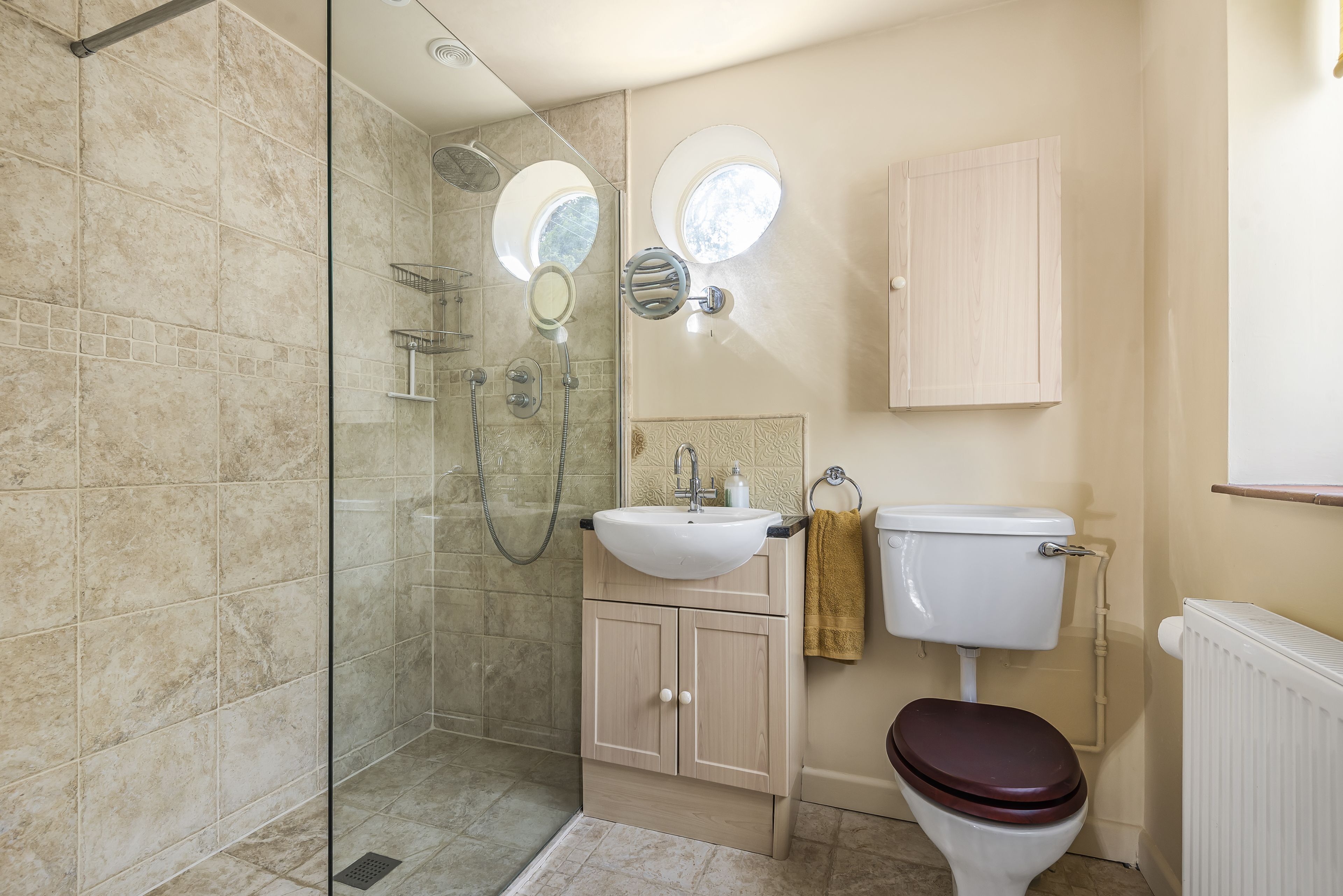 A bathroom with a glass-enclosed shower, a sink with a mirror, a toilet, and a cabinet.