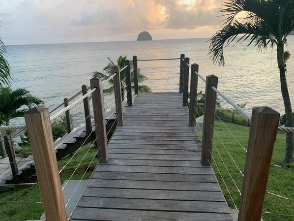 Une promenade en bois qui mène à une plage, d’où l’on peut admirer l’océan et une île lointaine.
