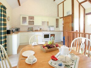 A dining area with a table set for two, a fruit basket, and a kitchen in the background. - Twinkles Cottage-UK12900 (Pelynt, near Looe)