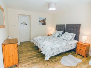 A bedroom with a bed, bedside tables, a wooden dresser, a door, and a painting on the wall.