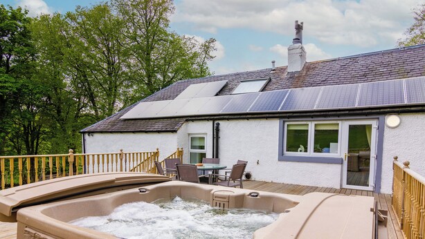 A hot tub with a stone facade, a deck, and a house with solar panels and a chimney. - Keepers Cottage - UK30246 (Glenshee, Cairngorms)
