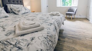 A neatly made bed with floral bedding, a grey upholstered headboard, and a chair by a window with a view of greenery. - Keepers Cottage - UK30246 (Glenshee, Cairngorms)