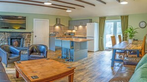 A modern kitchen with a stone fireplace, a dining area with a wooden table and chairs, and a living room with leather sofas and a coffee table. - Keepers Cottage - UK30246 (Glenshee, Cairngorms)
