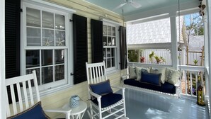 A covered porch with white rocking chairs and a swing seat, featuring a ceiling fan and starfish decorations. - Old Town Classic with plenty of charm, porch swing and parking (Key West)