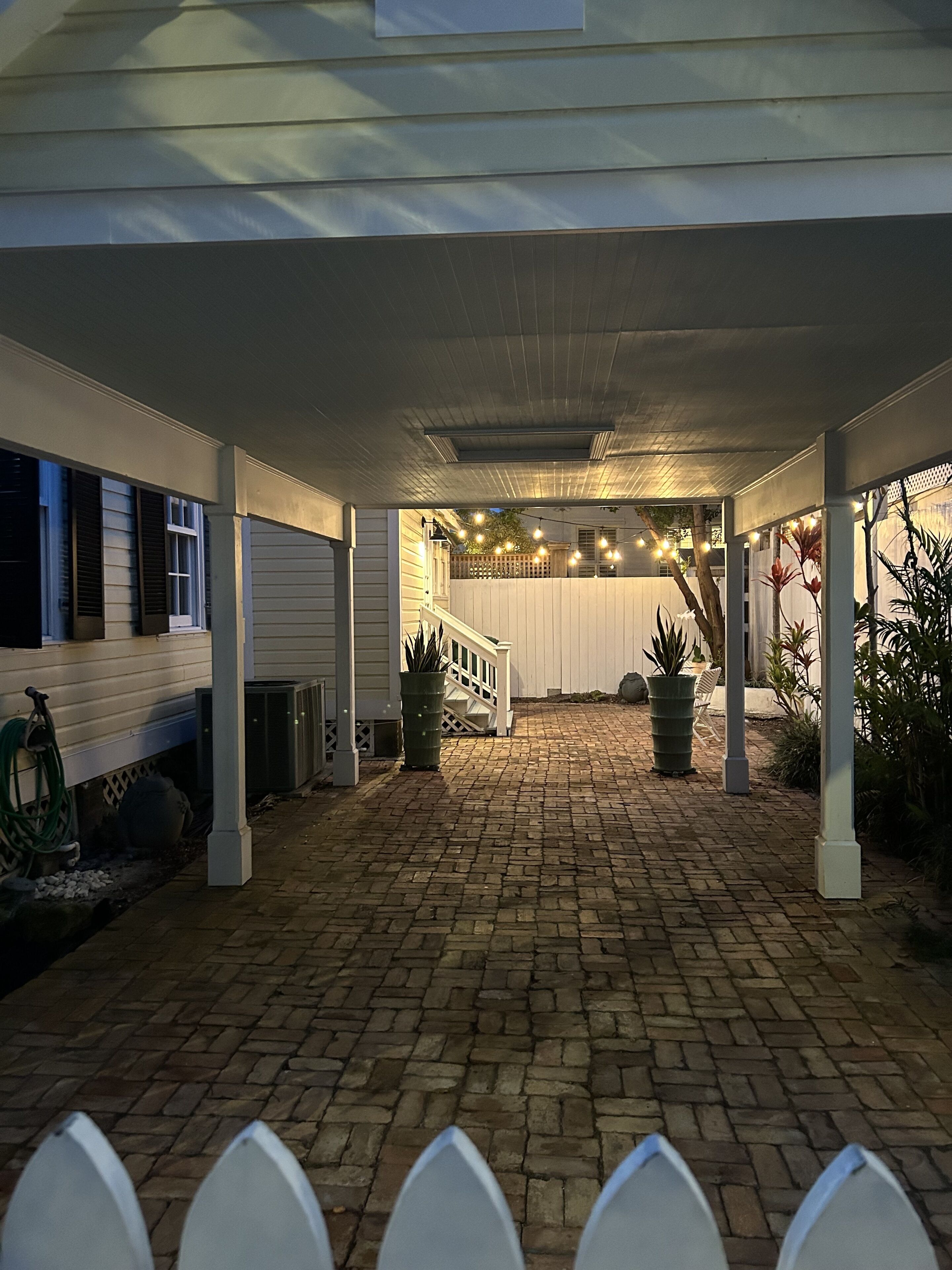 A covered patio area with brick flooring, white columns, and string lights.