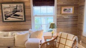 A cozy living room with a wooden wall, a white sofa, a wicker chair, and a window with a view. - Old Town Classic with plenty of charm, porch swing and parking (Key West)