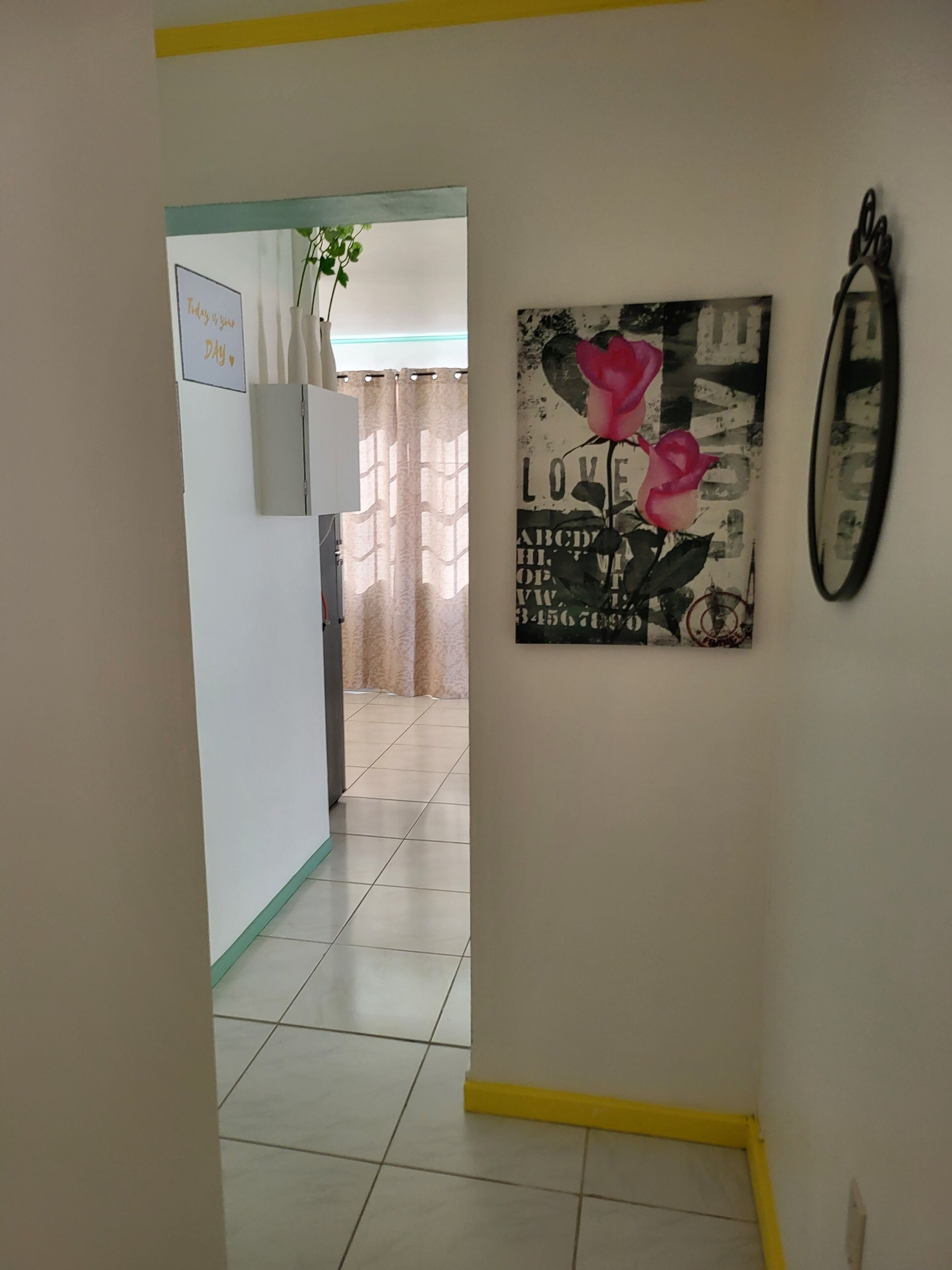 A hallway with a sign that says "Today is a good day." There is a framed picture of roses on the wall and a mirror.