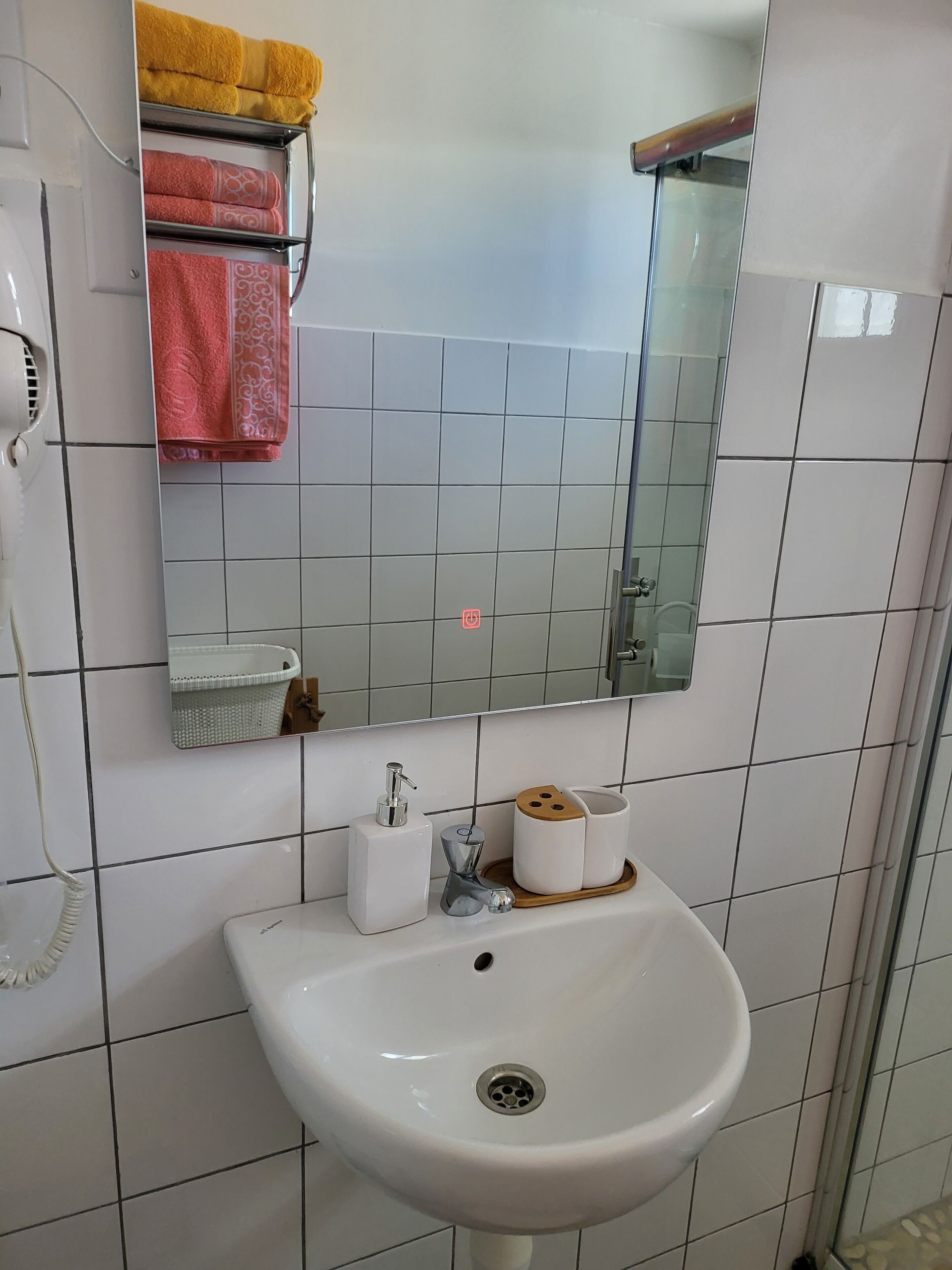 A bathroom with a white sink, a mirror, and a towel rack with yellow and pink towels.