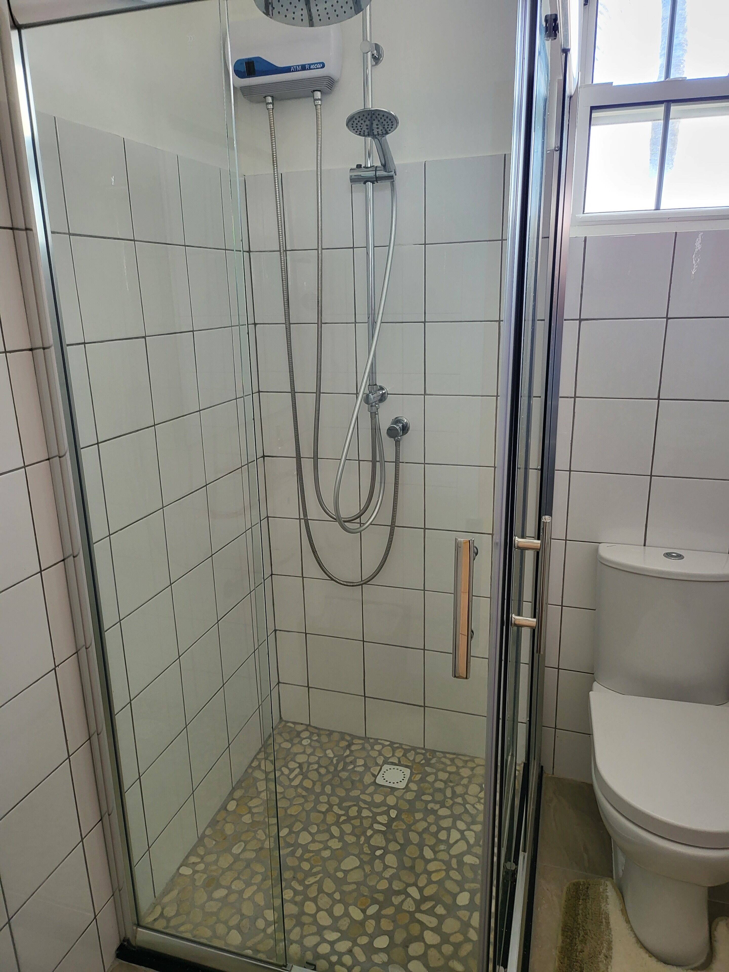 A glass-enclosed shower with a tiled floor, a toilet, and a window.